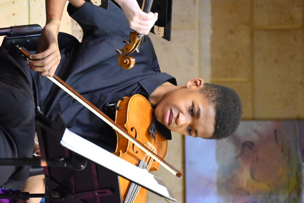 Young musician concentrating while playing violin in concert dress.